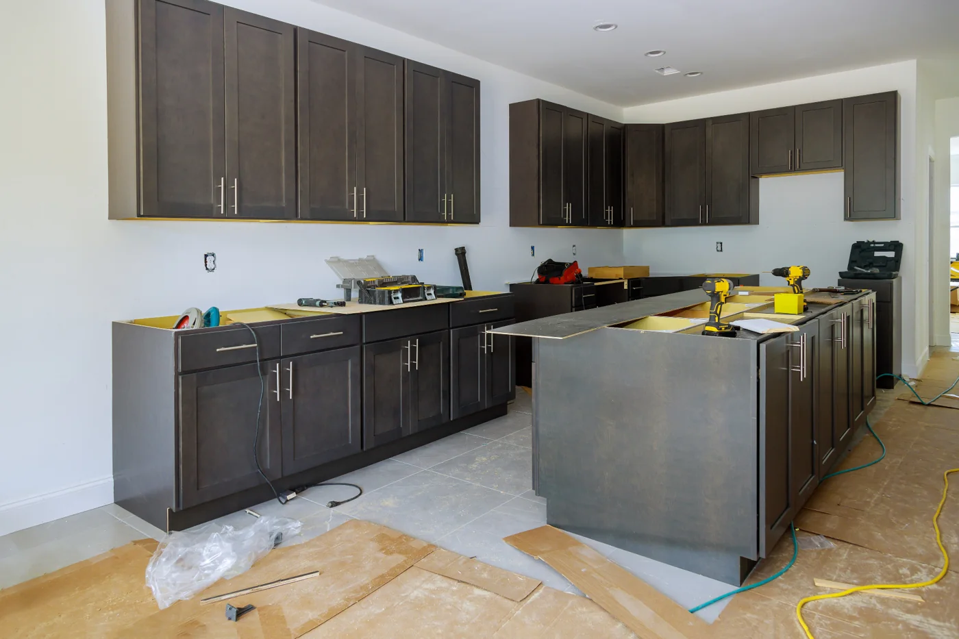 Kitchen cupboard installation example Dark kitchen cupboards and island cabinets being installed with tools and protective floor covering