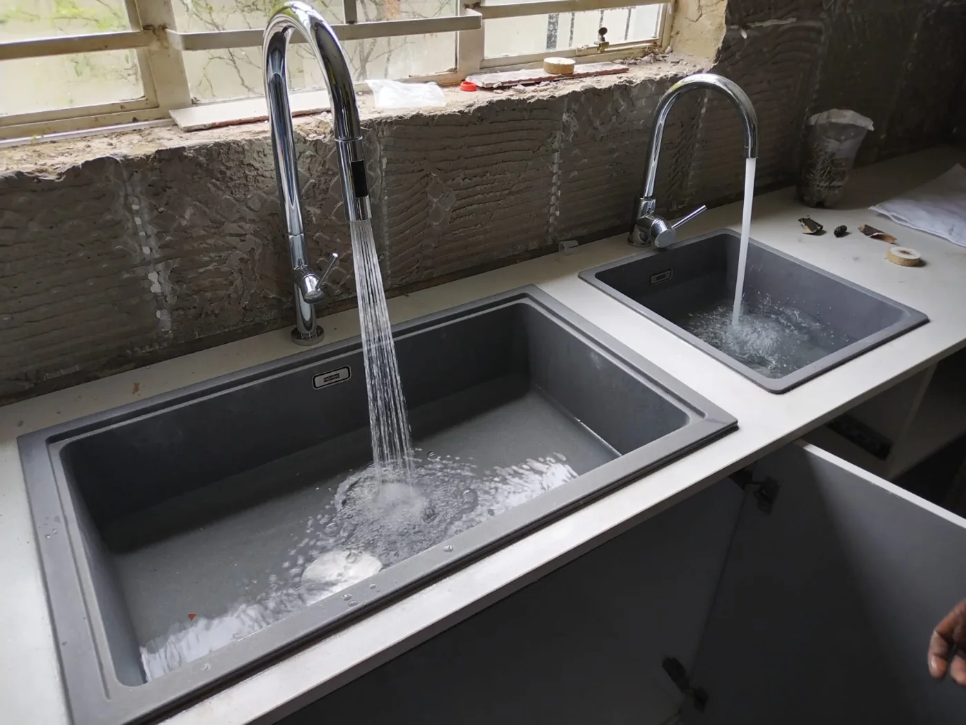 Kitchen renovation plumbing — Sink and mixer installation in progress Dark rectangular kitchen sink with a tall chrome mixer running water during installation