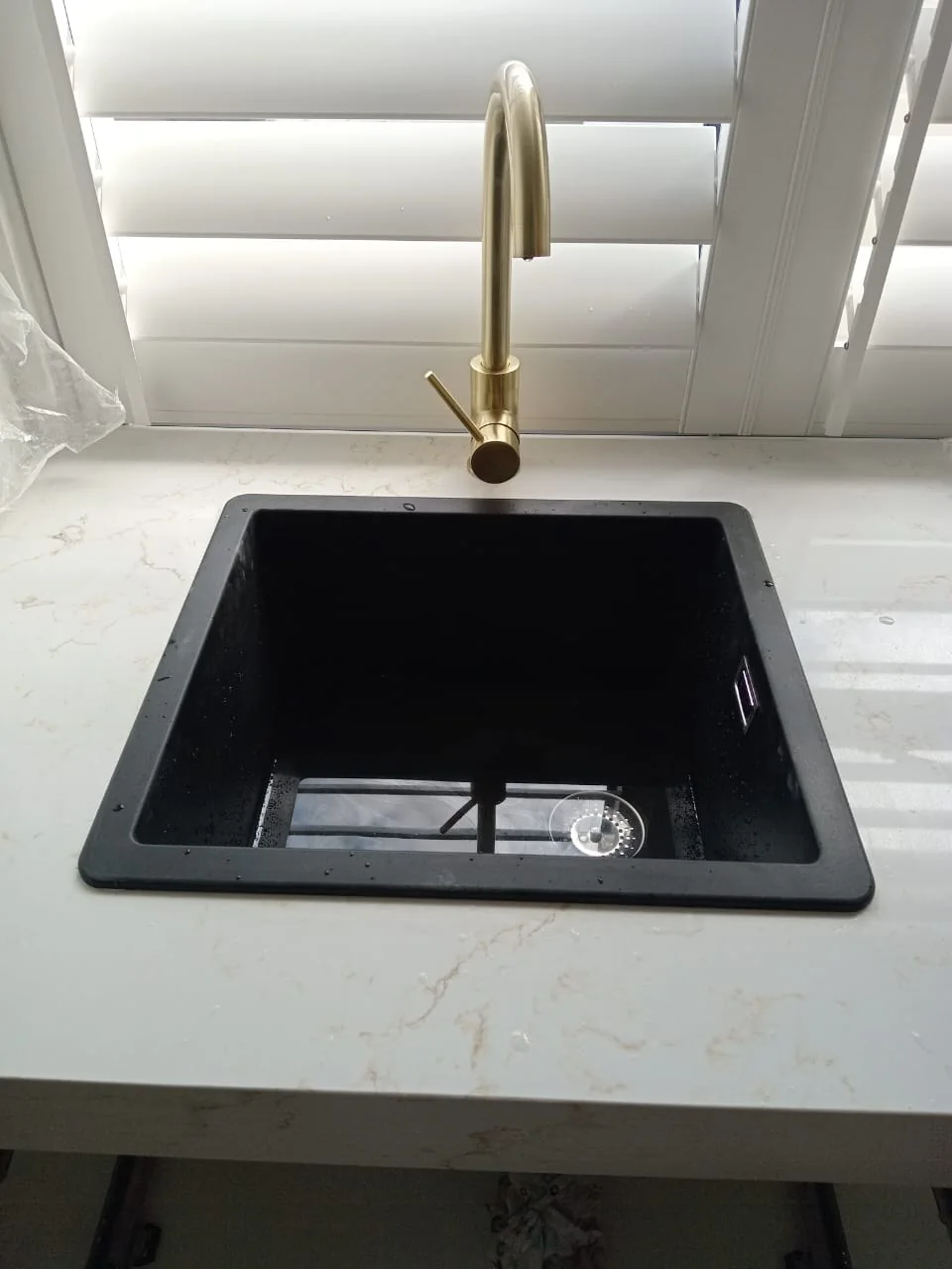 Small kitchen renovations — Compact single-bowl sink installation Single black kitchen sink with a gold-tone mixer set into a light worktop below a window