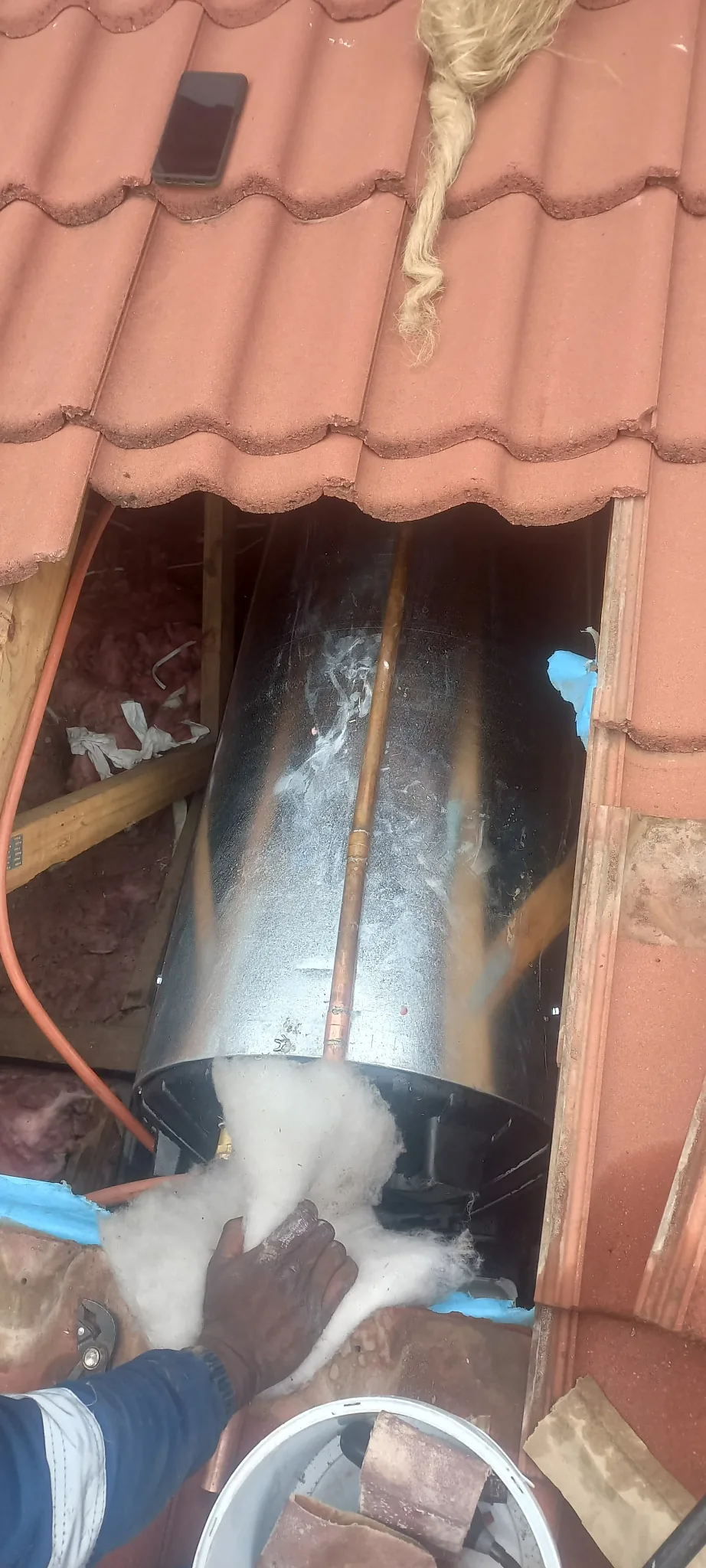 Replacement geyser being handled through a roof tile opening during burst geyser work