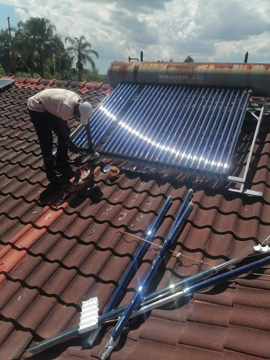 Plumber working on an evacuated tube solar geyser installed on a tiled roof