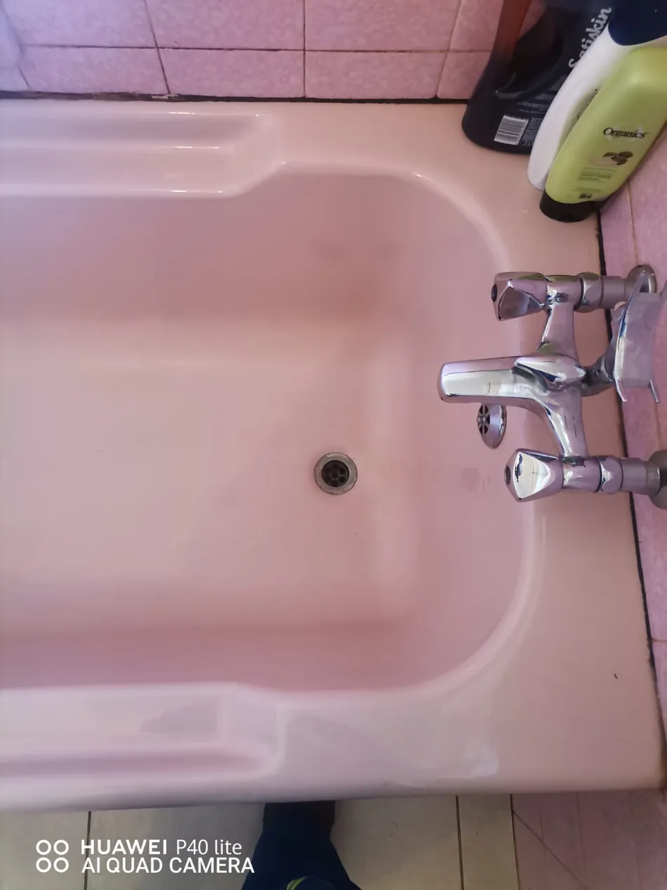 Pink bath with visible drain outlet and mixer taps