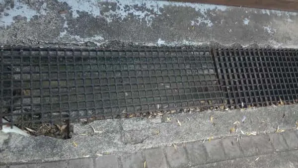 Outdoor stormwater channel grate beside paving with debris around the drain