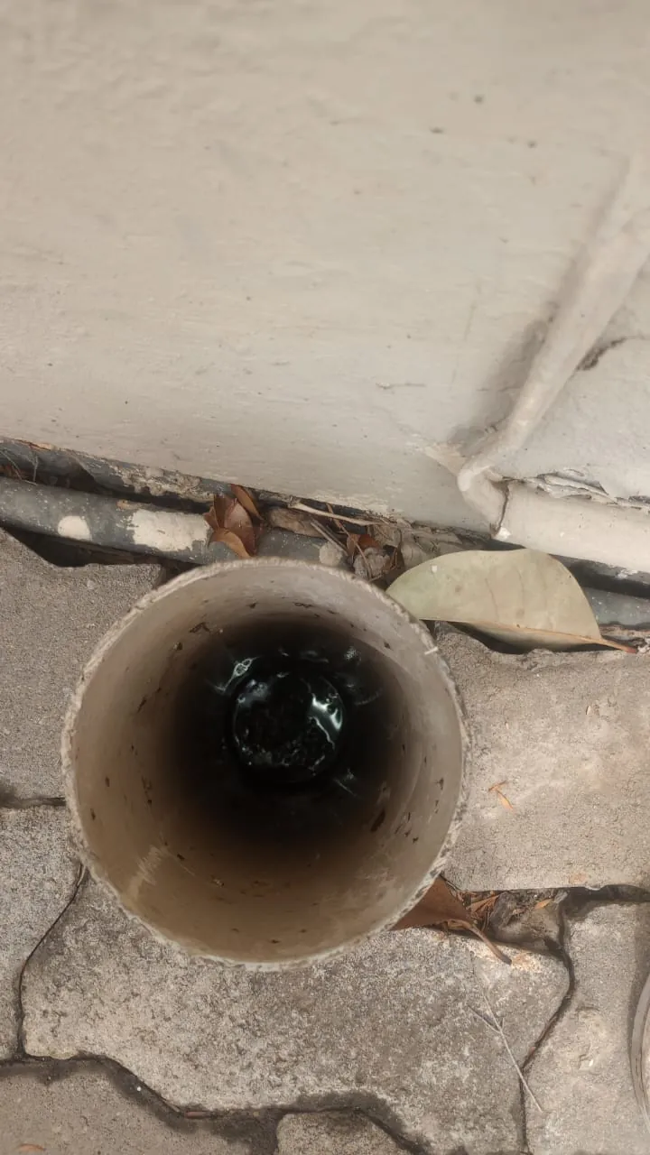 Open vertical drain access pipe with dark water visible inside near paving and a wall