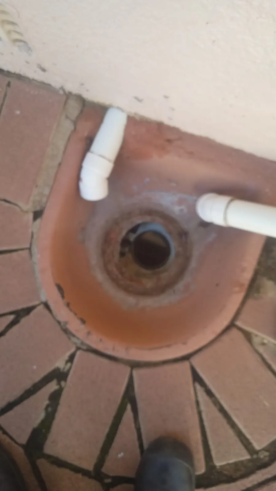 Open outside gully waste connection with white waste pipes entering the drain bowl
