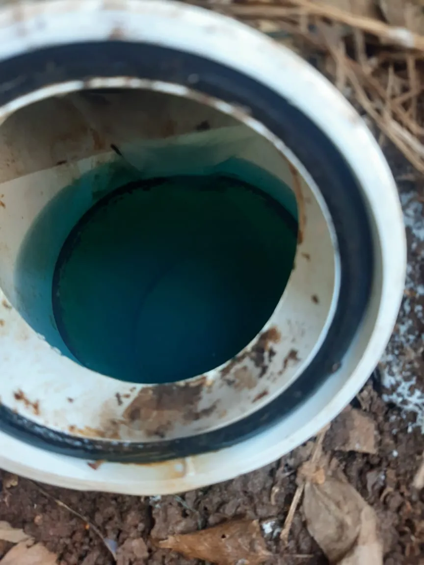 Open inspection pipe with blue-green standing water visible inside