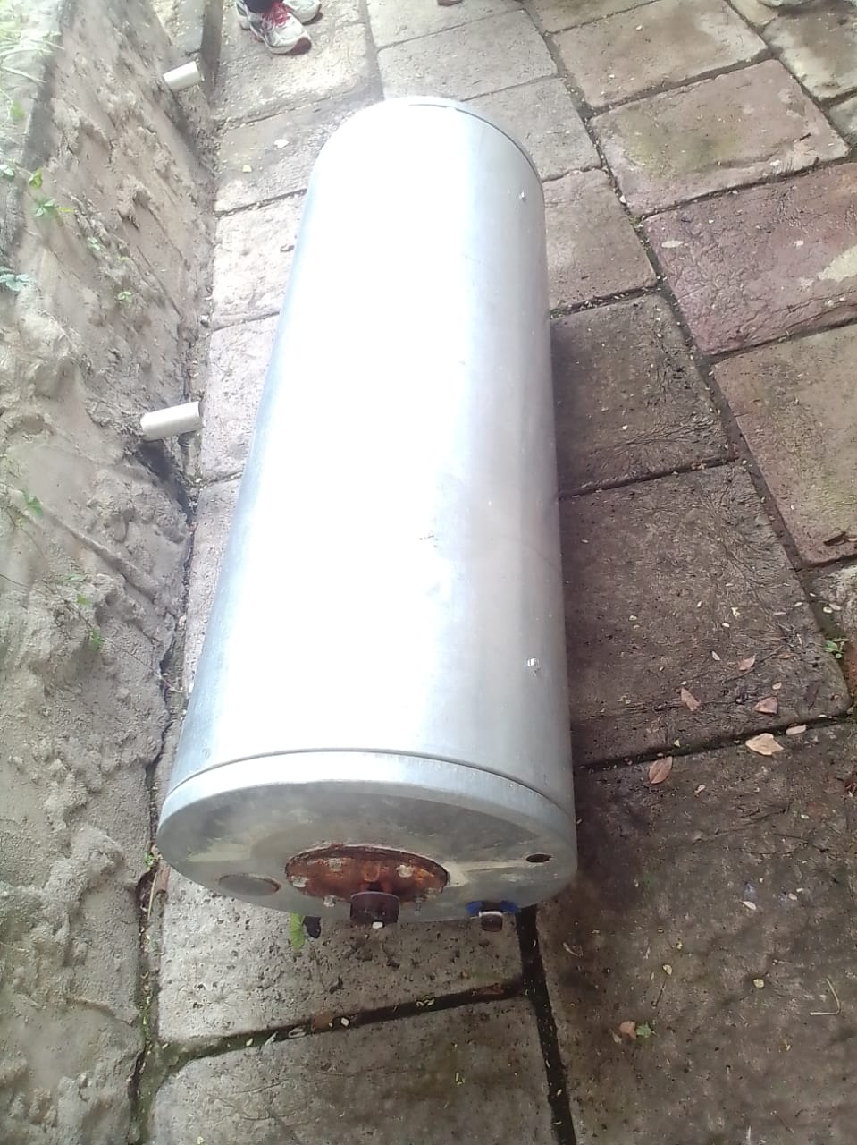 Burst hot water geyser removed and placed on paving in Elsburg, showing corroded base and damaged connections after failure, ready for replacement to restore reliable hot water supply and prevent further water damage.