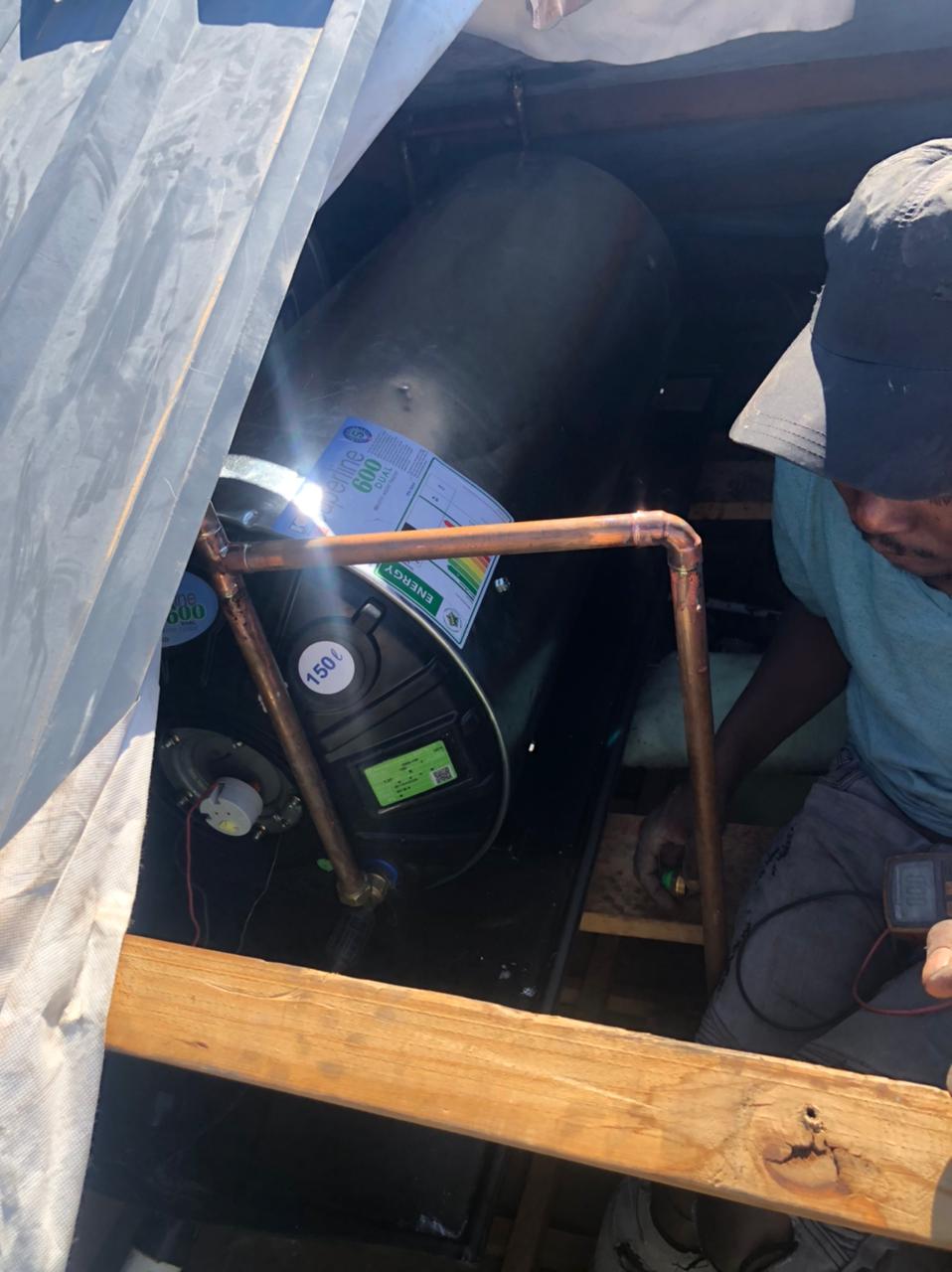 Burst geyser replacement in Ferndale, showing newly installed 150L geyser in ceiling space with copper pipework and technician completing installation to restore hot water supply.