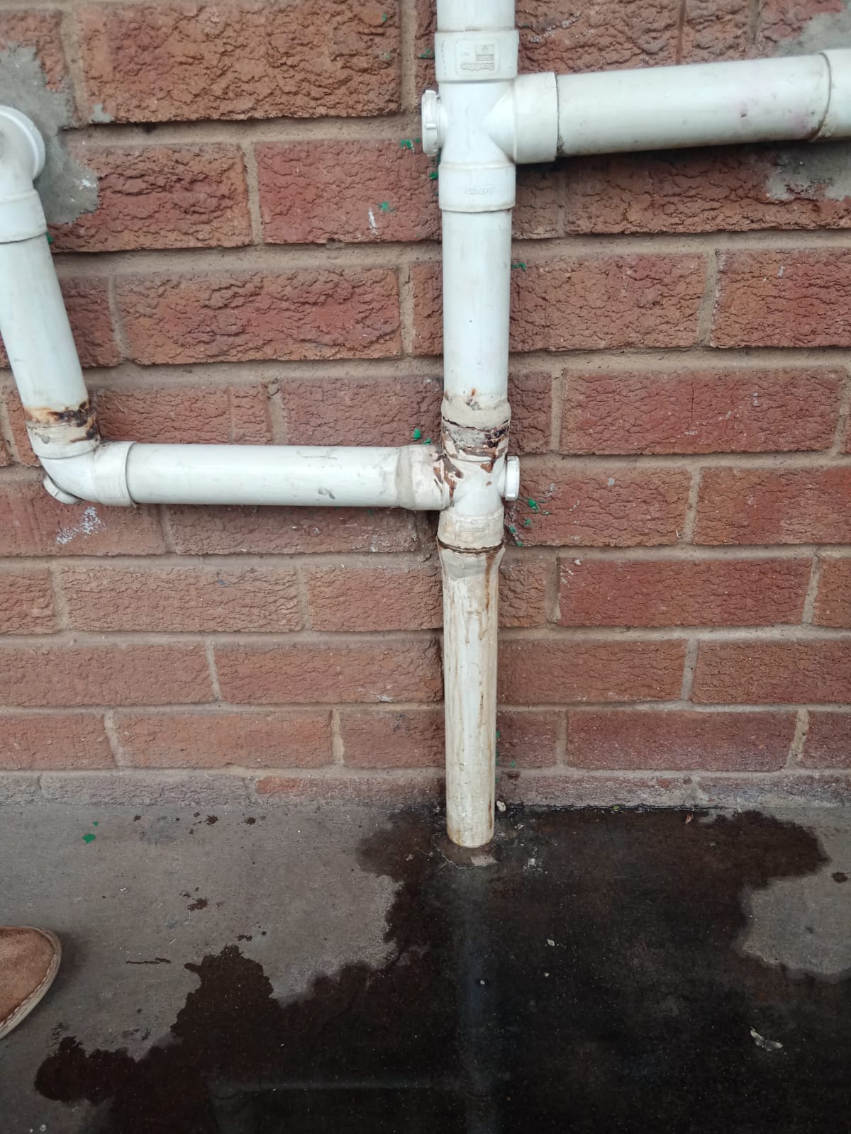 Faulty external waste pipe in Bedfordview leaking at joint against brick wall, with visible water pooling on ground below damaged connection, showing waste pipe requiring repair to stop leaks and restore proper drainage flow.