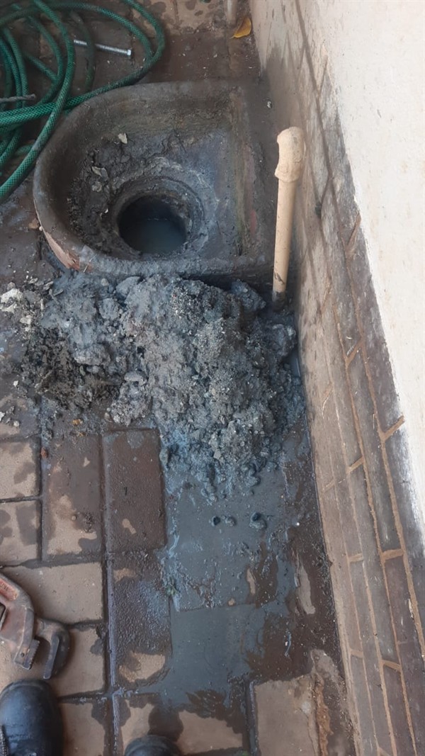 Plumber actively clearing a blocked drain pipe with tools visible