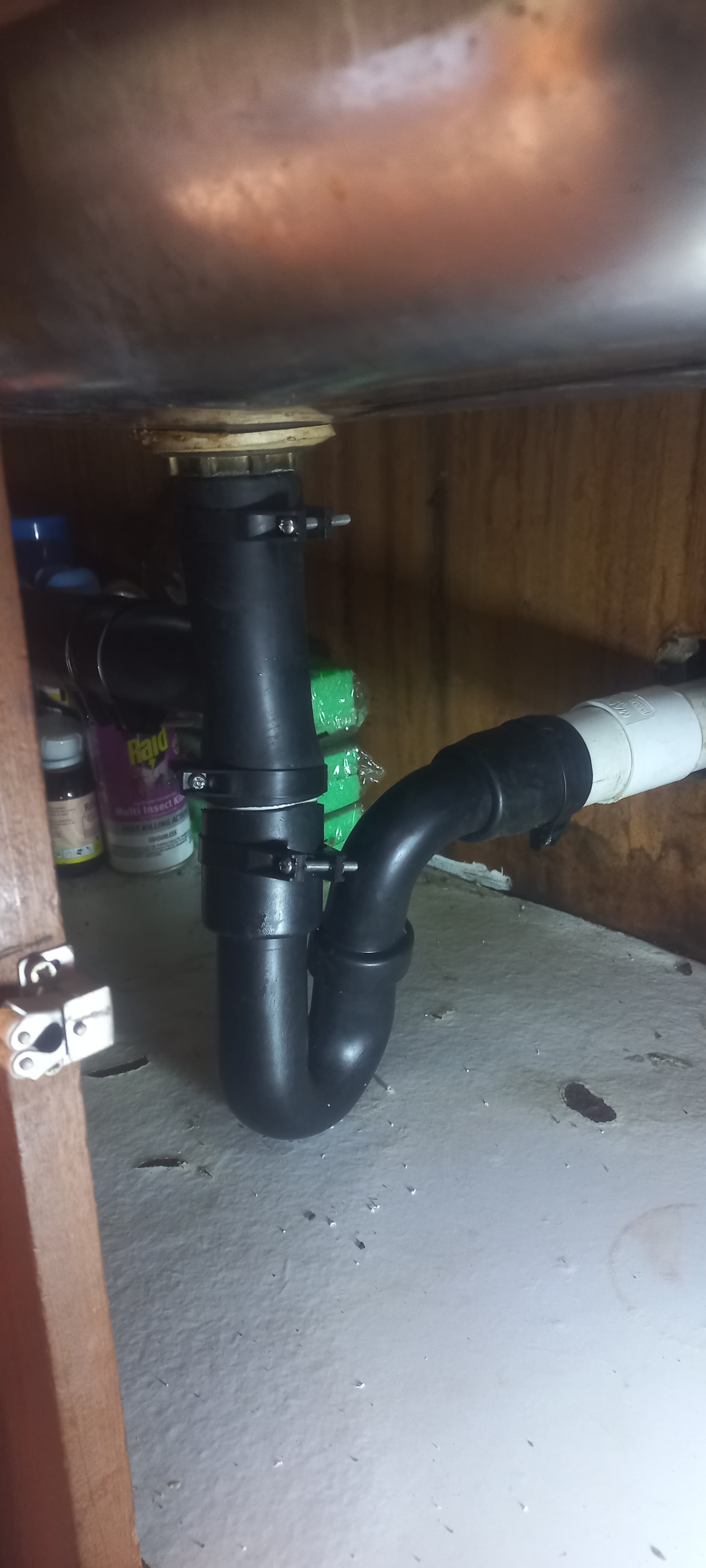 Newly installed black P-trap under kitchen sink in Glen Marais showing drainage pipe replacement and leak repair beneath stainless steel sink cabinet.