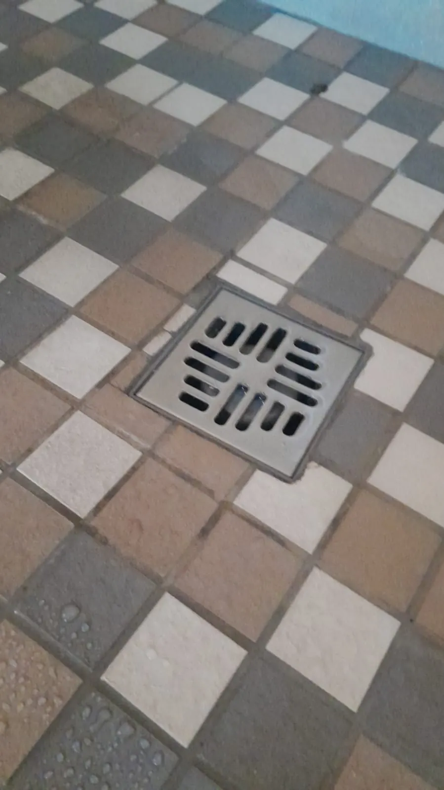 Square shower drain grate on tiled floor after blocked shower cleaning